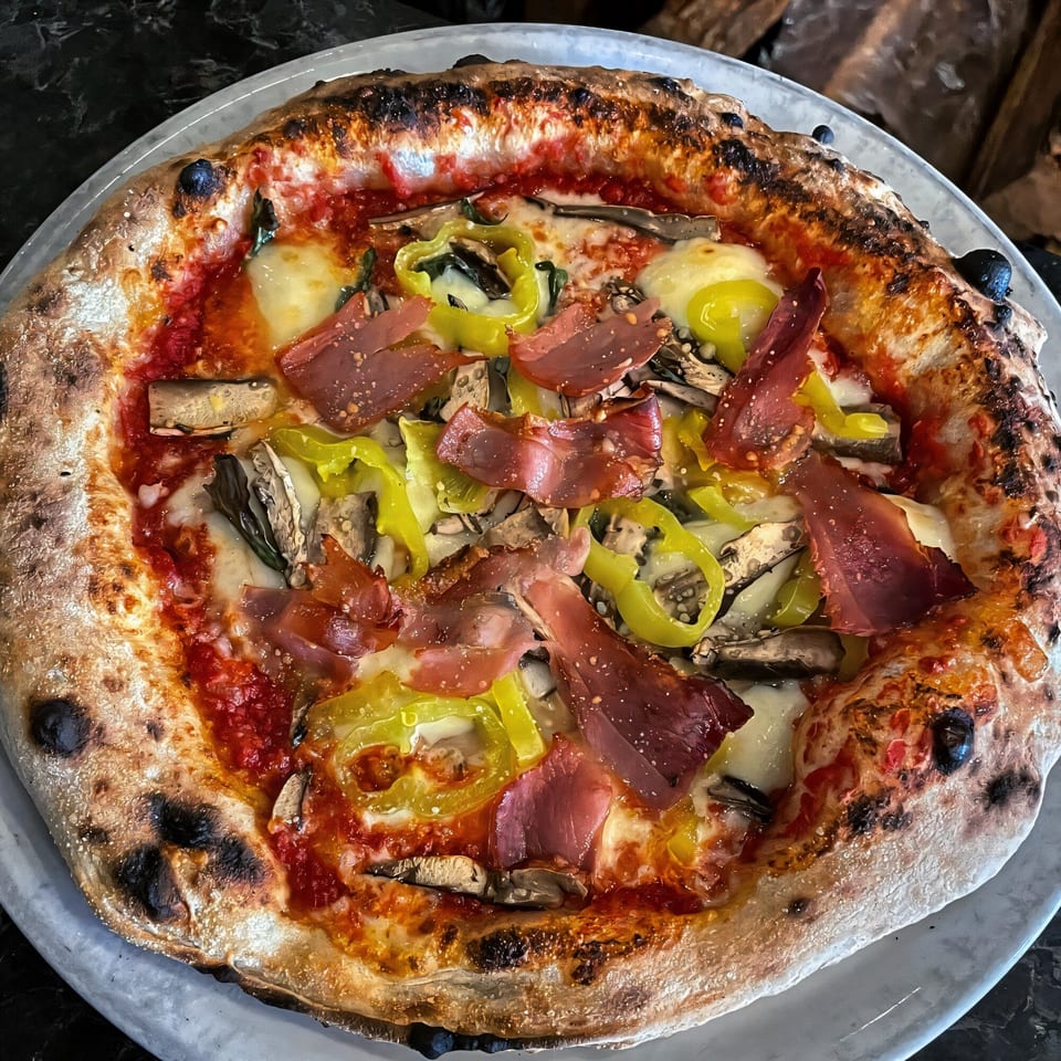 Aquila Pizza Al Forno's pizza with prosciutto, green peppers, mushrooms, and melted cheese.