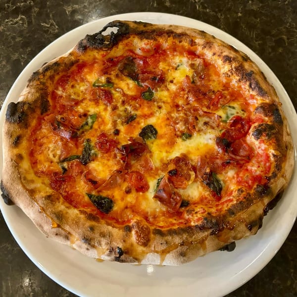 Aquila Pizza Al Forno's wood-fired pizza with melted cheese, tomato sauce, basil, and crispy crust.