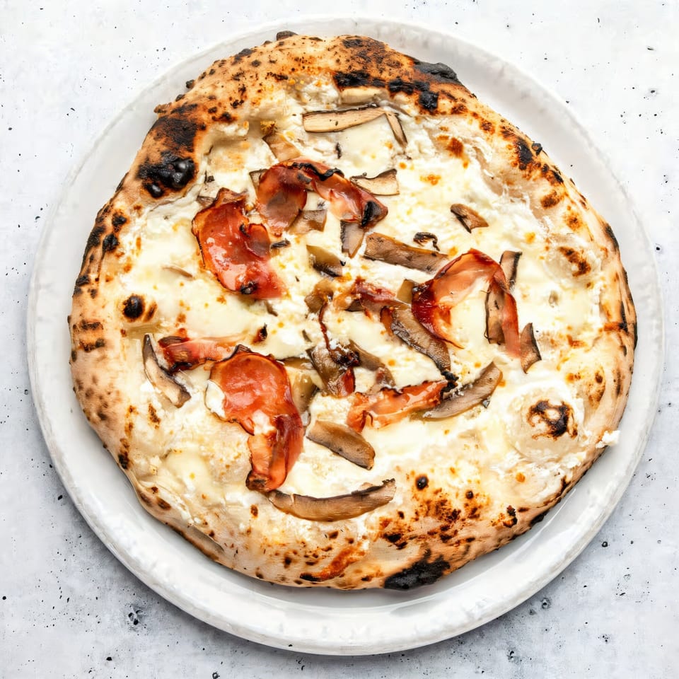 Aquila Pizza Al Forno's white pizza with prosciutto and mushrooms on a white plate.
