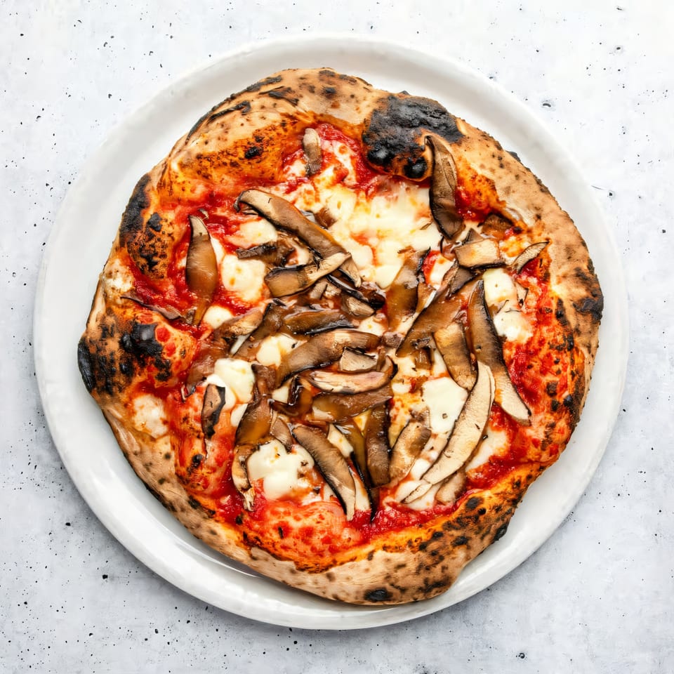Aquila Pizza Al Forno's mushroom pizza, with charred crust, tomato sauce, mozzarella, and sliced mushrooms.